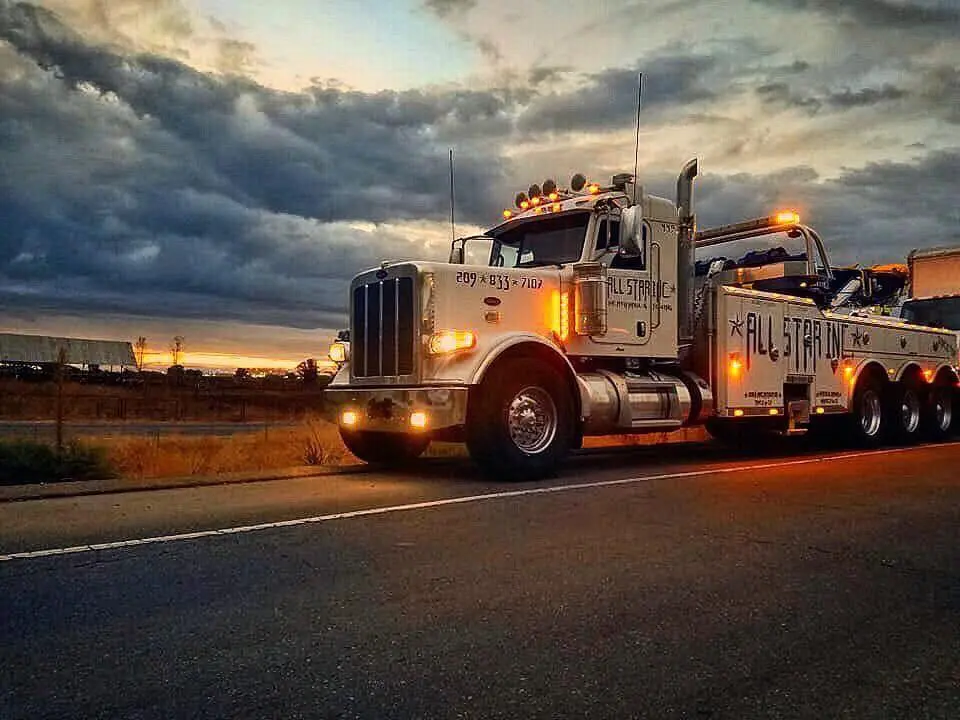 All Star heavy wrecker towing a semi truck along the I-5 freight corridor at speed.